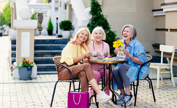 Three women are sitting at a table outside, laughing and enjoying each other's company.