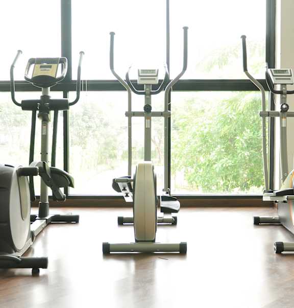 A row of stationary bikes are lined up in a row in a gym.