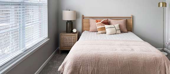 A bedroom with a bed, nightstand, and window with blinds.