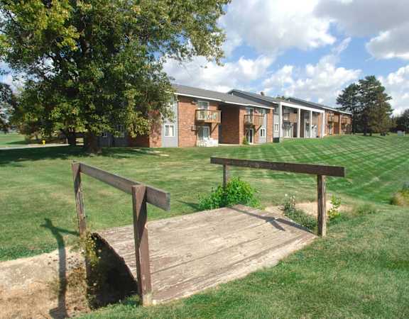 a wooden bridge in the grass in front of a building