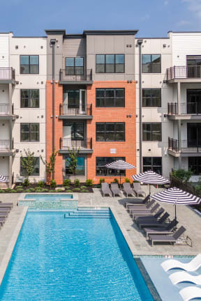 an outdoor pool with lounge chairs and umbrellas in front of an apartment building
