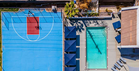 A basketball court is surrounded by a pool and lounge chairs.