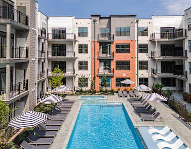 an outdoor pool with lounge chairs and umbrellas in front of an apartment building