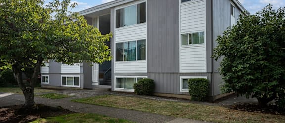 A grey building with white trim and windows is surrounded by greenery.