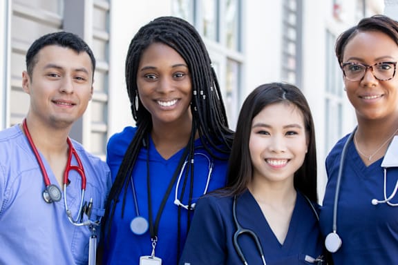 Four medical professionals in blue scrubs and stethoscopes stand together.
