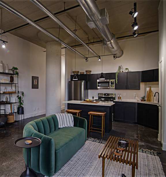 A living room with a green couch and a kitchen in the background.