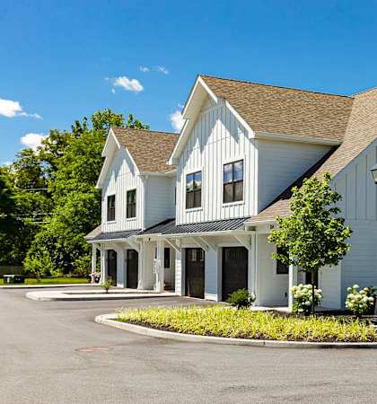 A white barn-style building with a brown roof and a porch.