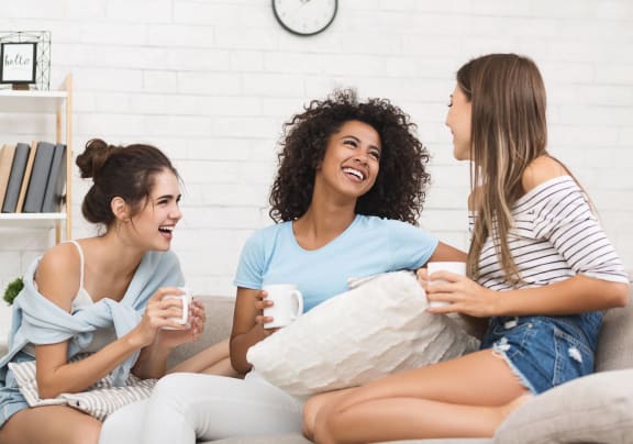 three women sitting on a couch holding coffee cups and a pillow at Altis Grand Kendall, Miami, FL