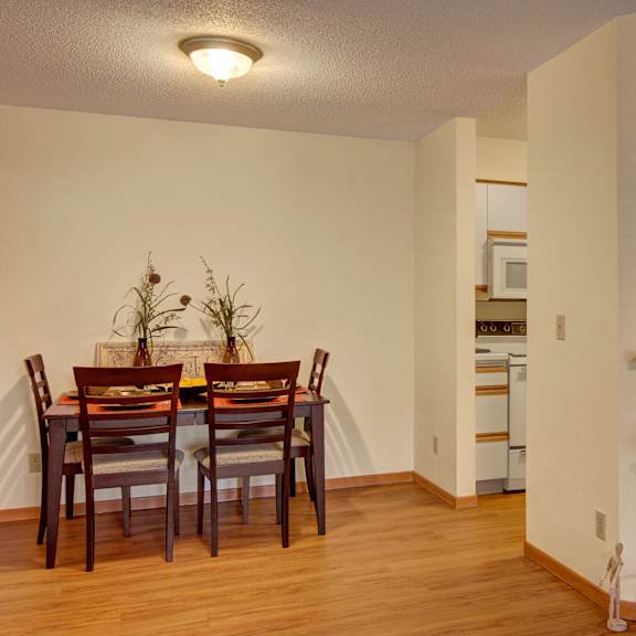 The all-white kitchen with decorations and plants and a view of the dining room with a table and four chairs and four places set at Town Centre Apartment Homes. 