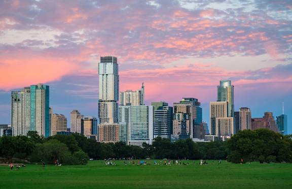 A city skyline at sunset with a green park in the foreground.