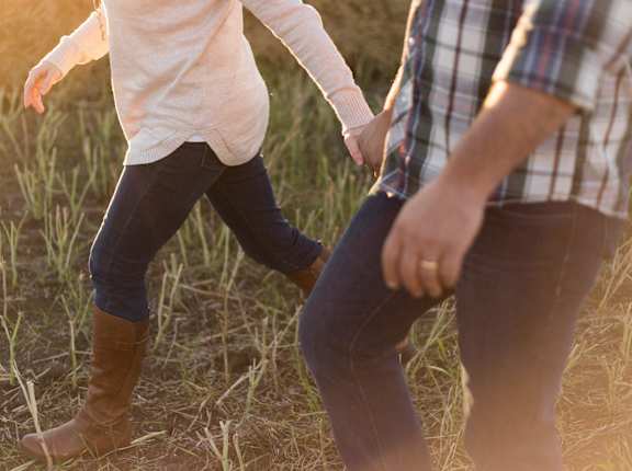 a couple holding hands while walking in a field