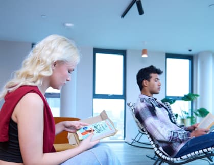 A man and a woman are sitting on a couch, each reading a book.