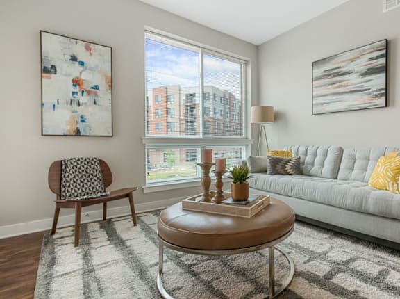 A living room with a grey couch, a wooden chair, a coffee table, and a large window.