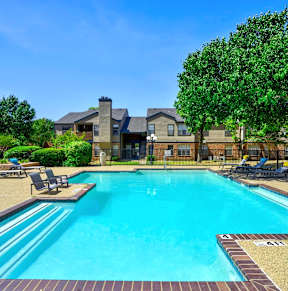 A swimming pool surrounded by trees and a house in the background.