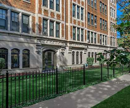 A tree stands next to a black fence in front of a building.