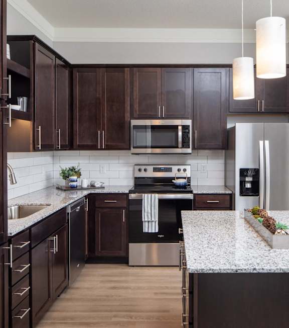 A kitchen with dark wood cabinets and a granite countertop.at The Edison at Spirit, Lakeville, MN