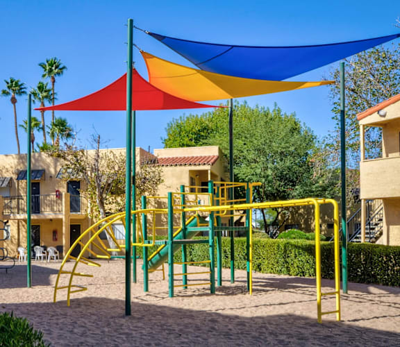 A playground with a yellow slide and a blue, red, and yellow shade structure.