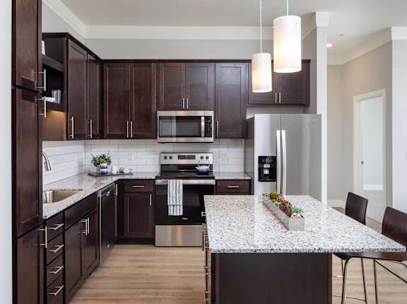 A kitchen with dark wood cabinets and a granite countertop.at The Edison at Spirit, Lakeville, MN 55044