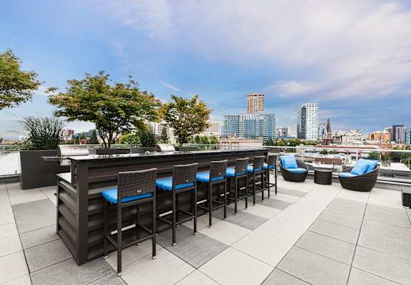 A rooftop bar with blue chairs and a view of the city skyline.