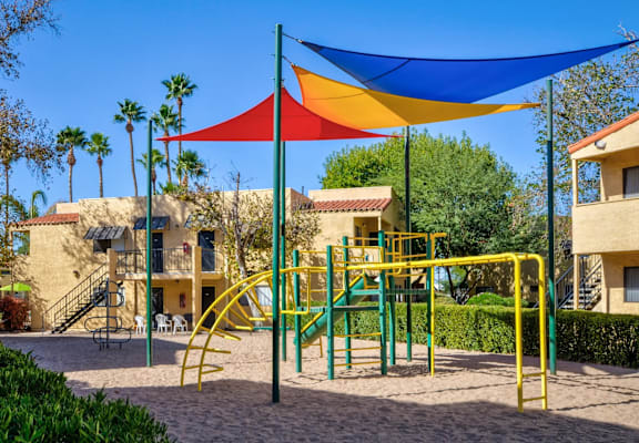 A playground with a yellow slide and a blue, red, and yellow shade structure.