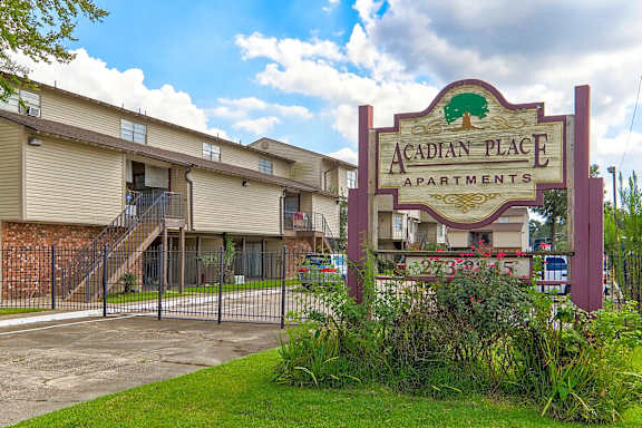 A sign for Acadian Place Apartments stands in front of a building.