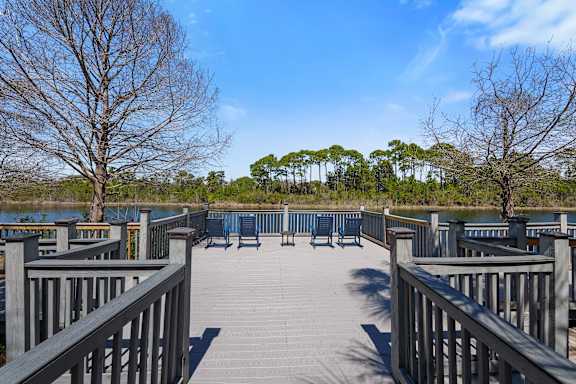 A wooden deck overlooking a body of water with benches and trees in the background.