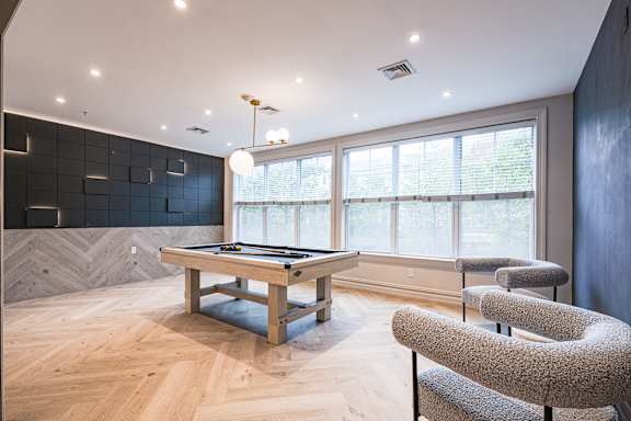 A billiard table is in the middle of a room with a blue rug and a chair with a grey cushion.