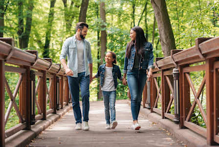 Three people are walking on a bridge in a wooded area.