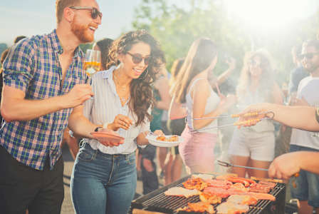A group of people are gathered around a barbecue grill, enjoying food and drinks.