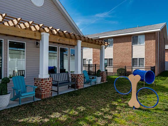 A dog bone sculpture is in the front yard of a house with a wooden pergola.