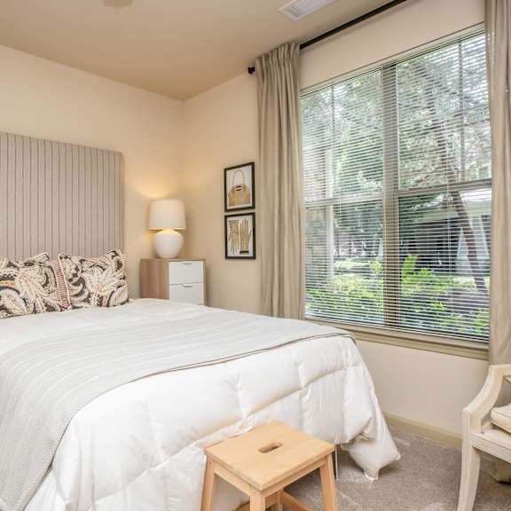 A bedroom with a large bed, a window with curtains, and a chair.