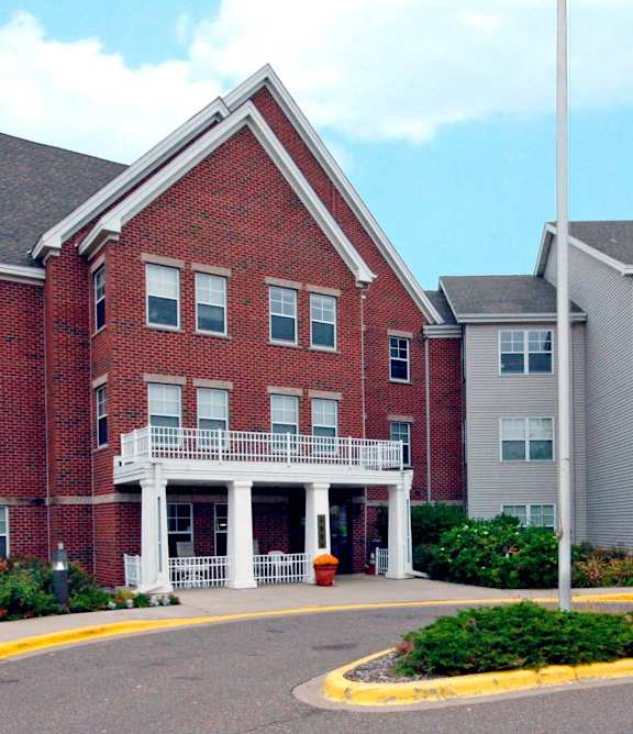 A red brick building with a white porch and a grey building to the right.