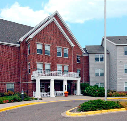 A red brick building with a white porch and a grey building to the right.