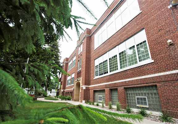 A red brick building with green plants in front.