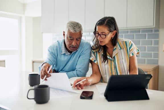 A man and woman are looking at paperwork together at a table.