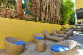 Community Lounge Area with Wicker Seats with Blue Cushions, Wicker Lounge Chairs, Trees, and Yellow Wall at Croft Plaza Apartments, West Hollywood