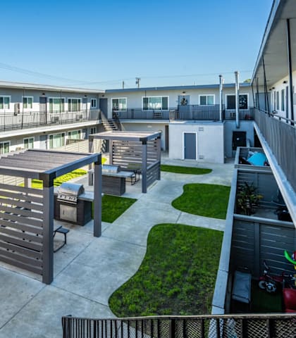 A sunny day at the outdoor patio of a building with a grill and picnic table.