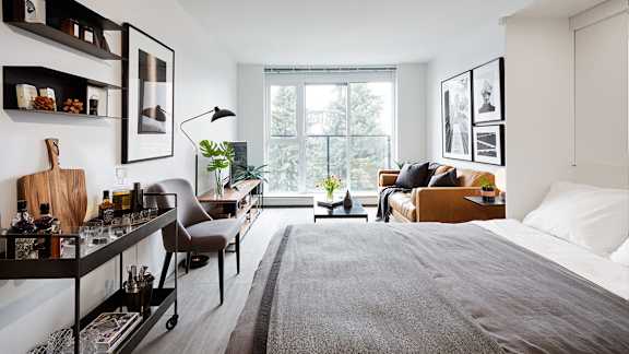 A well-lit bedroom with a large bed and a small kitchenette.