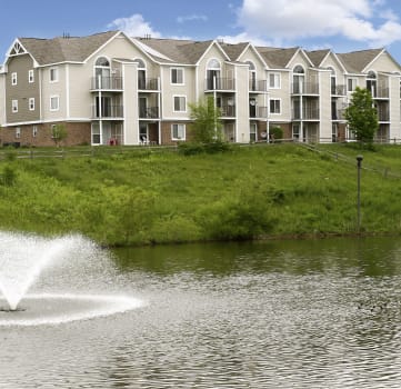 a fountain in a pond with an apartment building in the background