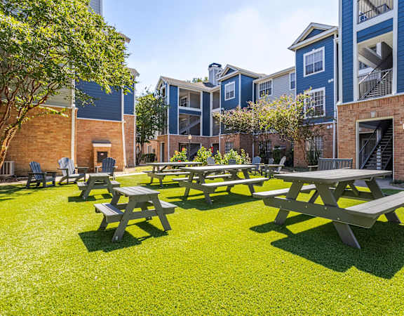Lush outdoor picnic area with benches, greenery, and modern apartment buildings at Gramercy Park Apartments.