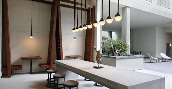 A long white table with stools is in a room with a white ceiling and a white wall. at G12 Apartments, Los Angeles, CA, 90015