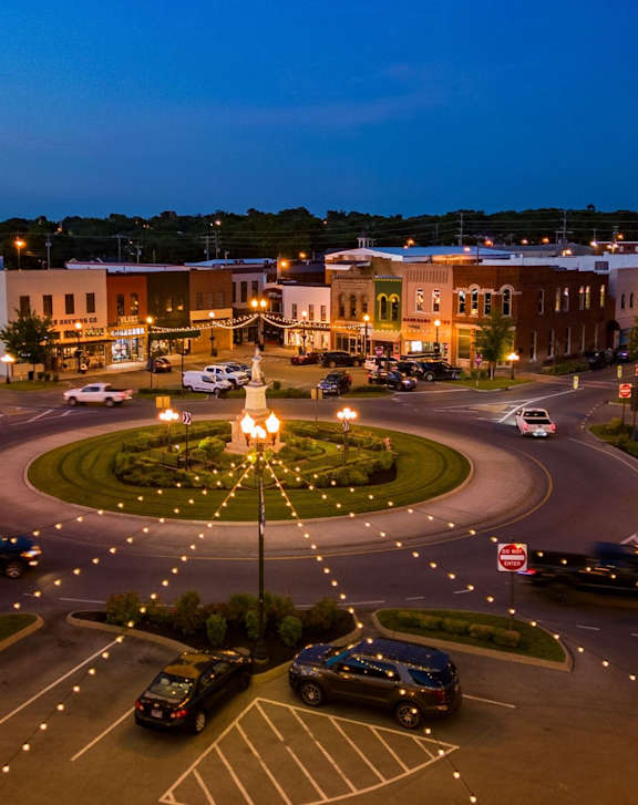 A roundabout with cars and buildings around it at night.
