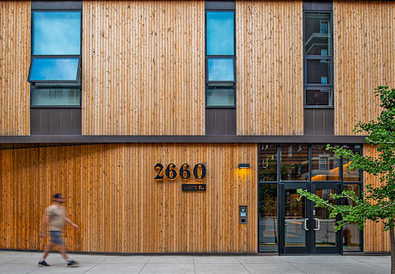a man walking in front of a building with wooden facade and glass windows