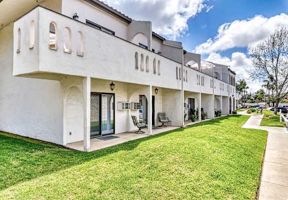 A white building with a balcony and a green lawn in front.