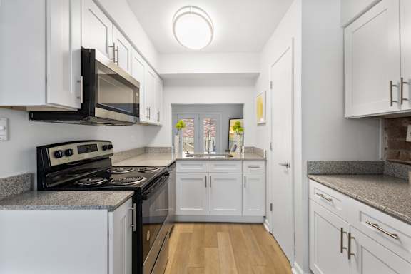 Modern galley kitchen at Monon Living in Broad Ripple featuring white shaker cabinets, granite countertops, and pass-through window with Monon Trail access nearby.