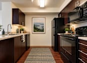 Thumbnail 1 of 8 - A kitchen with black appliances and a painting of a lake on the wall.