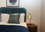 Thumbnail 4 of 7 - a bedroom with a bed with a blue blanket and a nightstand with a lamp