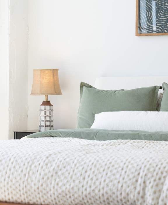 A bed with a white comforter and green pillows is in the image.
