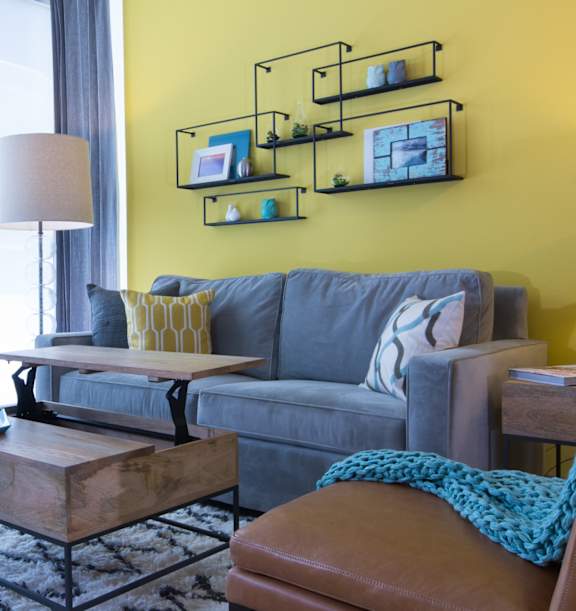 A living room with a grey couch, a wooden coffee table, and a yellow wall.
