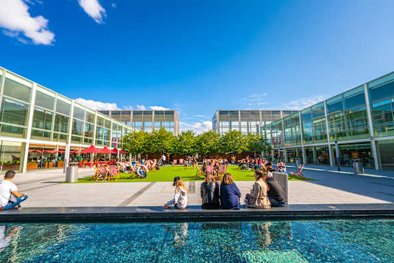 People are sitting by the pool in a sunny outdoor area. at The Woodlands Apartments, Milton Keynes, MK5 6GS